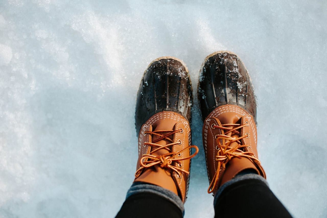 Brown leather and rubber lace-up winter boots standing on fresh white snow