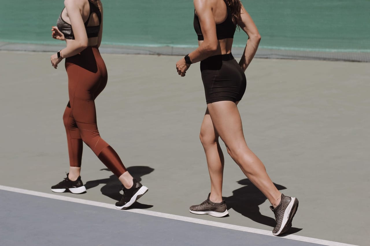 Two women in sportswear and sneakers walking in step across a sunlit outdoor court