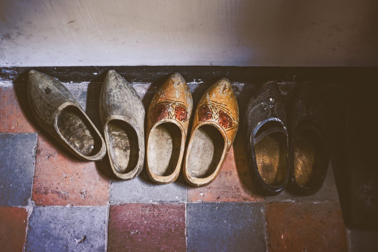Three pairs of wooden clogs lined up in a row on a tiled floor
