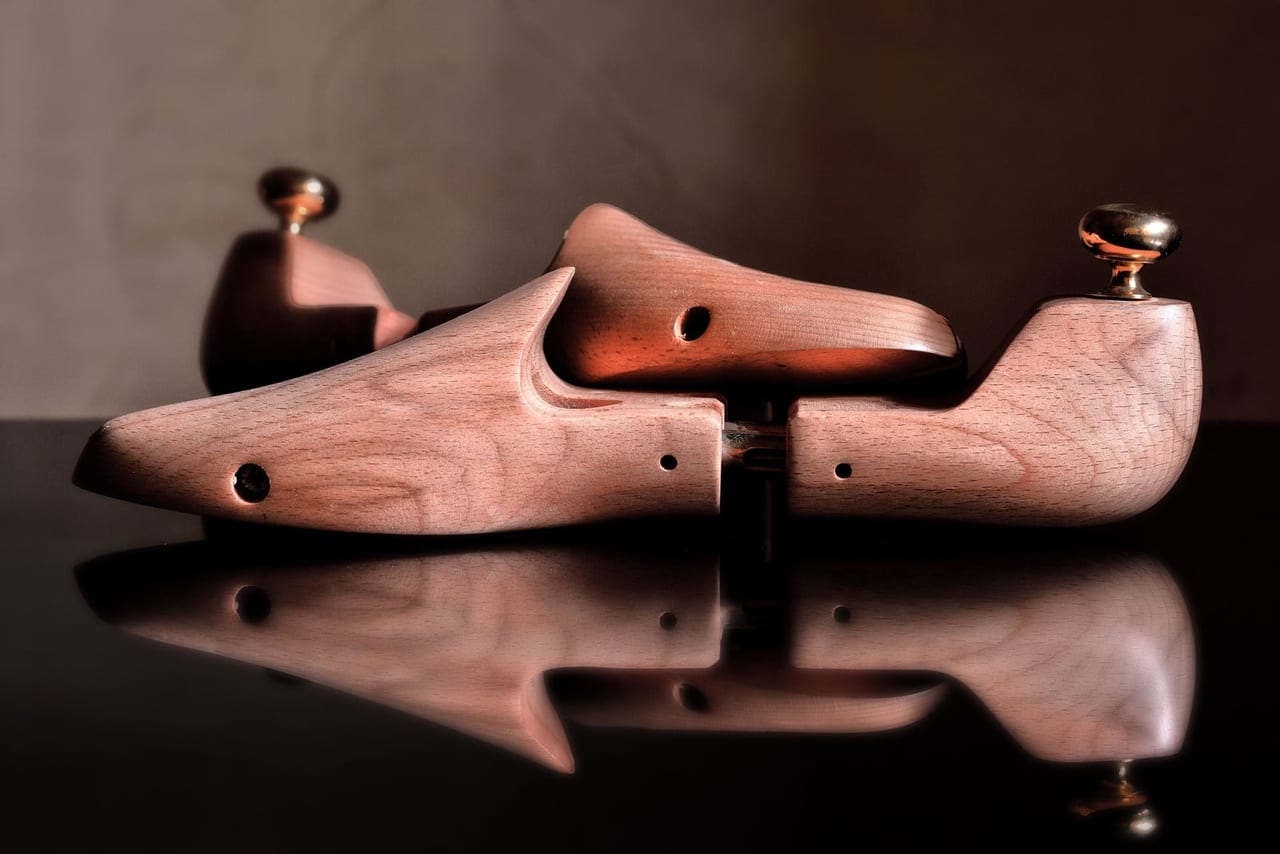 Two wooden shoe trees with brass knobs on a glossy black surface, reflected below