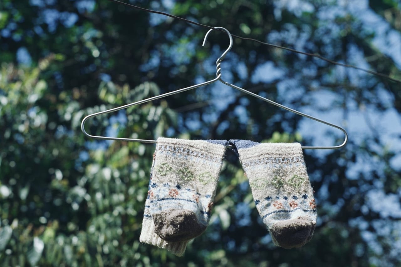 Pair of patterned wool socks drying over a wire hanger outdoors under trees