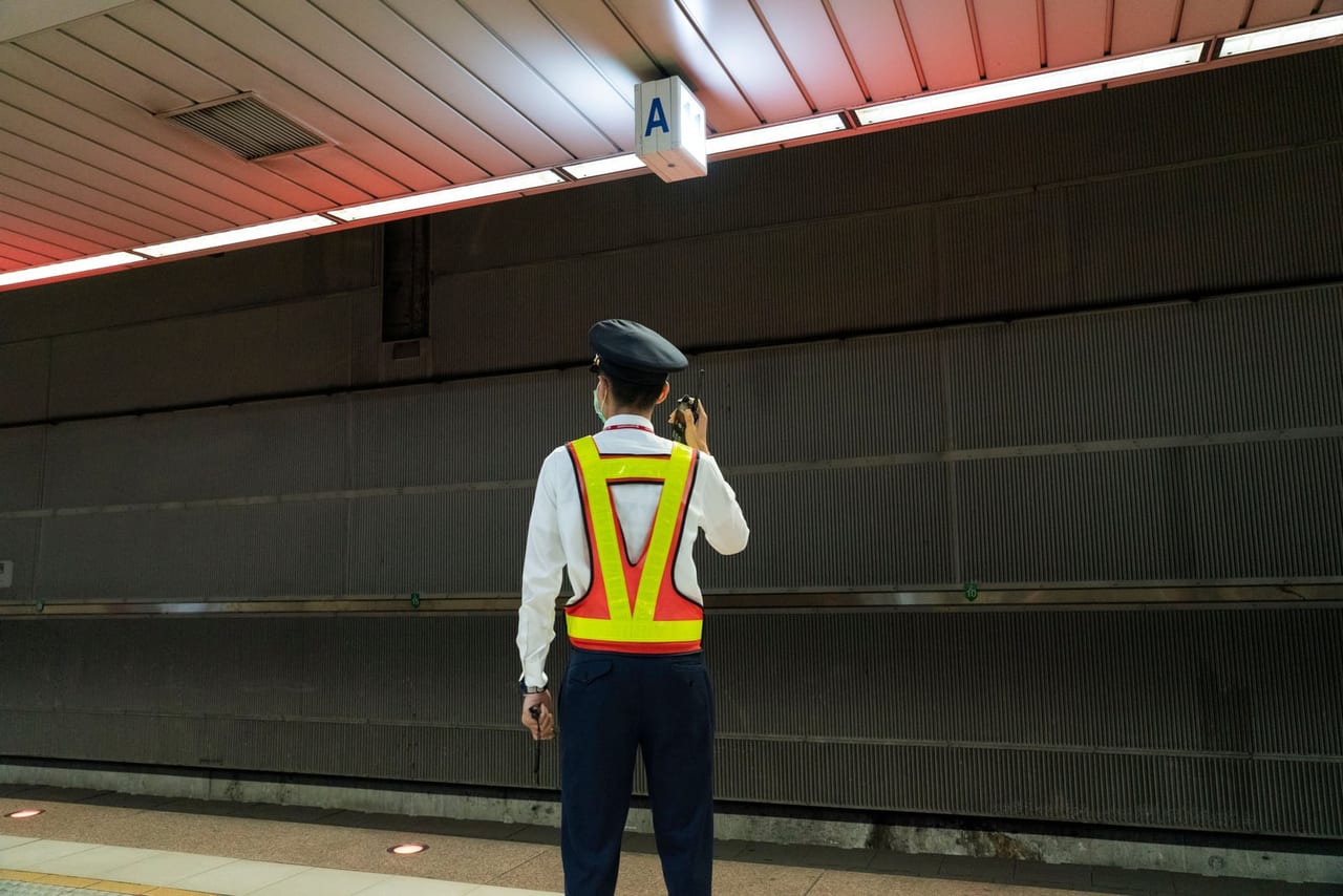 Uniformed worker in a reflective vest using a radio on an empty train platform