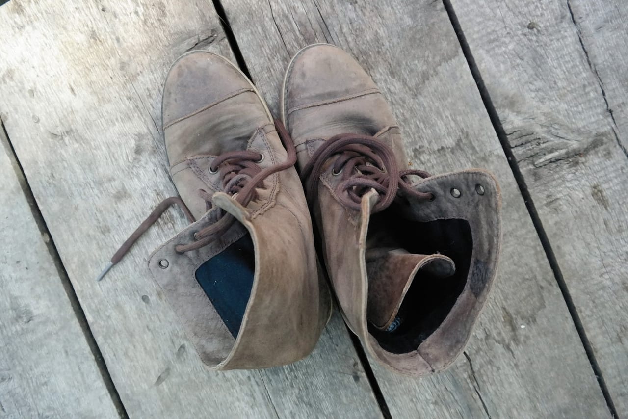 Pair of worn leather boots with loosened laces on weathered wooden planks, seen from above
