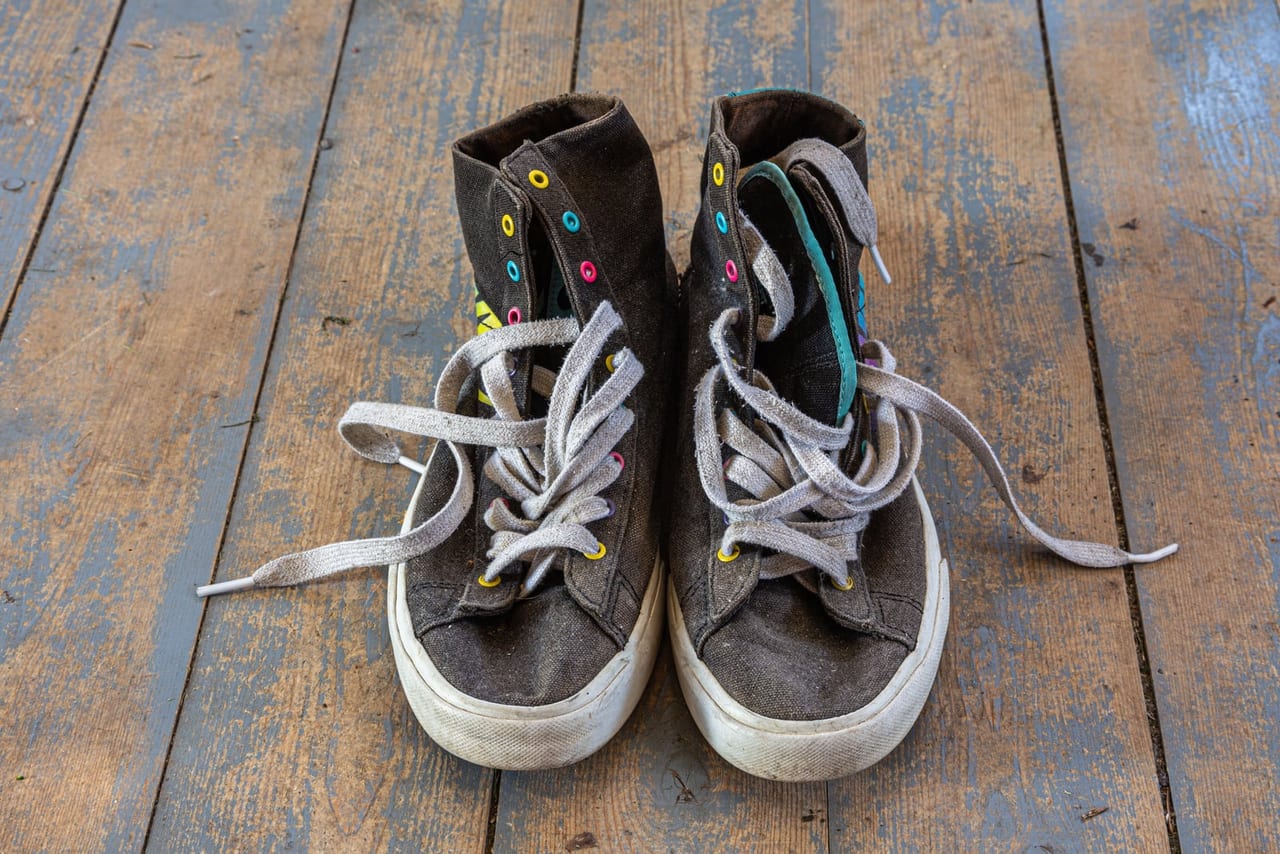 Well-worn dark canvas high-tops with colorful eyelets and loose laces on weathered floorboards