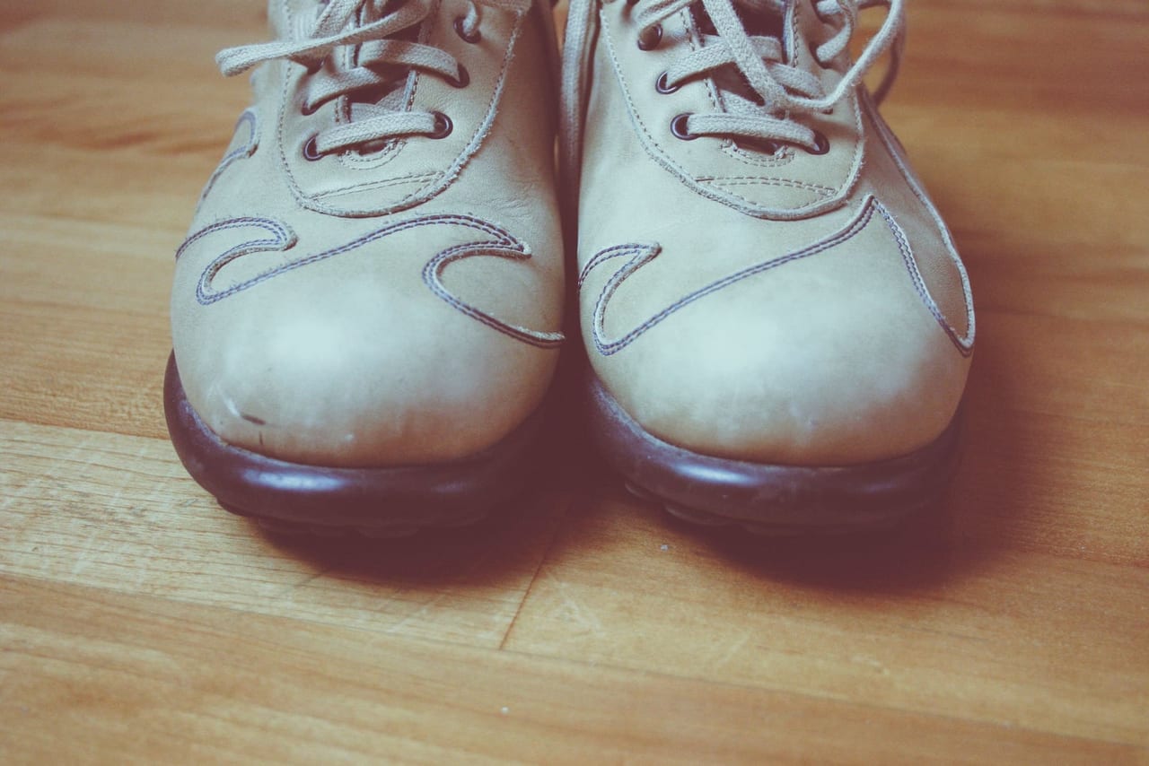 Pair of worn beige leather lace-up shoes with scuffed toes on a wooden floor