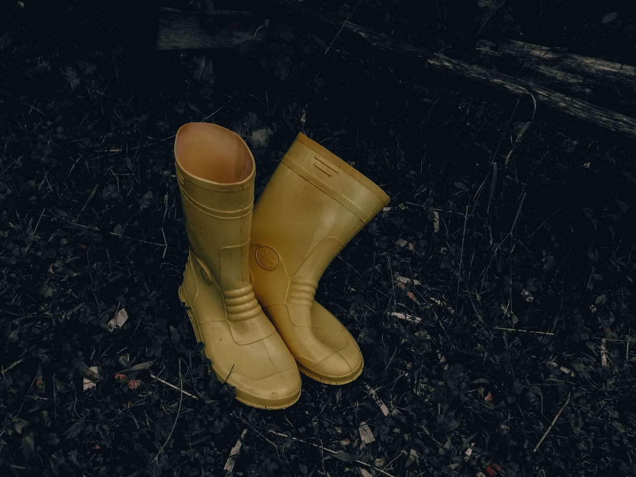 A pair of yellow rubber boots standing upright on dark ground